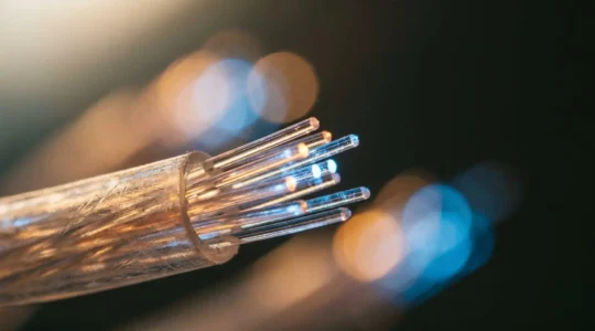 Close-up of illuminated fiber optic cables transmitting data streams with bokeh light particles representing high-bandwidth 4K streaming network