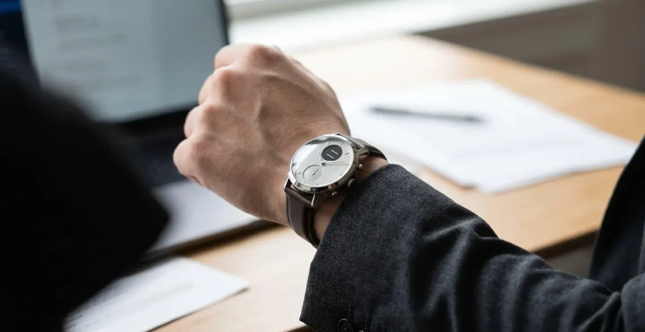 Close-up of a hybrid smartwatch with analog hands on a professional wrist in an office setting
