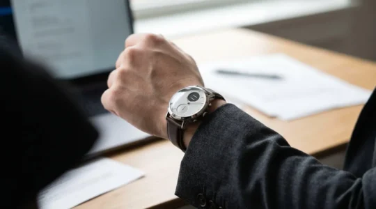 Close-up of a hybrid smartwatch with analog hands on a professional wrist in an office setting