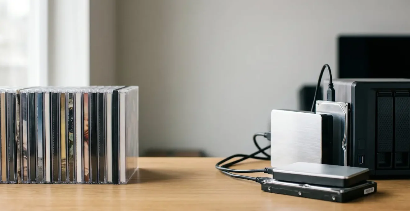 Professional photo of vintage CD collection alongside modern external hard drives showing digital music archiving transition