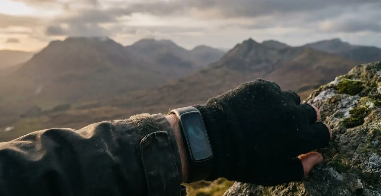 Athlete checking wearable fitness tracker on mountain summit in Scottish Highlands during altitude training